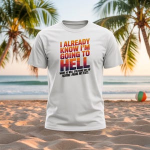 May include: White t-shirt with the text "I ALREADY KNOW I'M GOING TO HELL" in a gradient of orange, red, and purple. The shirt also includes the text "MIGHT AS WELL STIR SOME SHIT UP BEFORE I MAKE MY EXIT!"