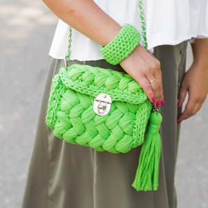 May include: A green crocheted handbag with a silver clasp and a green tassel. The bag is worn over the shoulder with a silver chain strap.