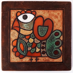 Może przedstawiać: Kwadratowa płytka ceramiczna z ilustracją stylizowanego ptaka z dużym białym okiem, pomarańczowo-zielonym upierzeniem i ciemnobrązową drewnianą ramą. Tło płytki ma cętkowaną beżową teksturę z wyraźnymi czarnymi konturami definiującymi postać ptaka.