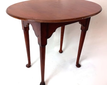 Op de afbeelding: Een ronde, donkerbruine houten tafel met een glad oppervlak. De tafel heeft vier slanke, taps toelopende poten. De tafel is ongeveer 76 cm in diameter en 71 cm hoog.