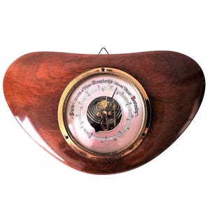 May include: A wooden barometer with a brass face and a white dial. The dial has black markings and red text that reads "Storm" and "Bestendig".