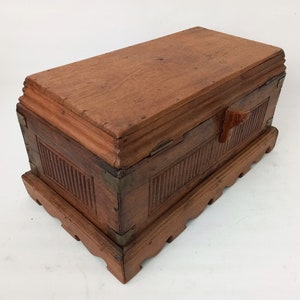 May include: A wooden box with a hinged lid and a carved wooden handle. The box has a decorative base with a scalloped edge. The box is made of dark wood and has a natural finish.