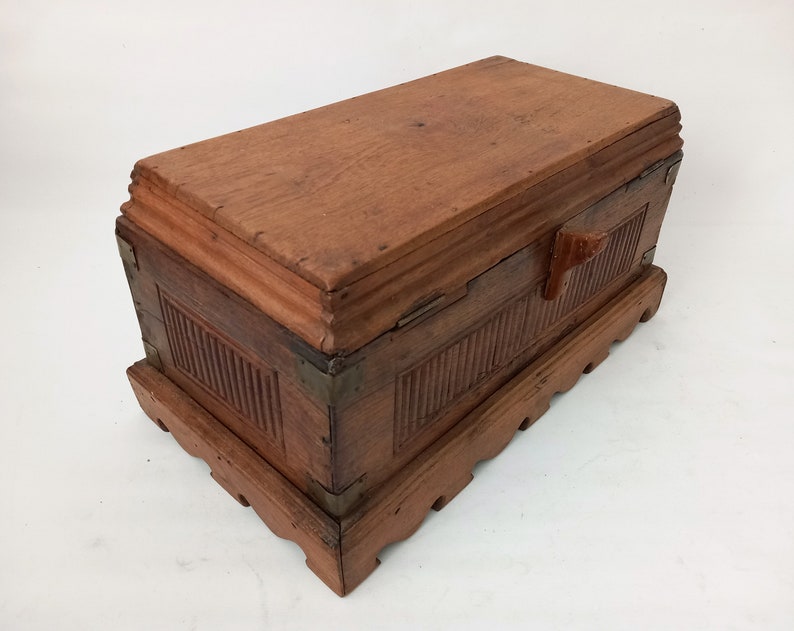 May include: A wooden box with a hinged lid and a carved wooden handle. The box has a decorative base with a scalloped edge. The box is made of dark wood and has a natural finish.