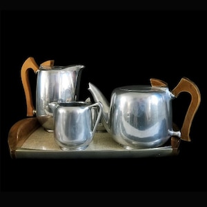 Puede incluir: Un juego de té de plata con asas de madera en una bandeja de madera. El juego incluye una tetera, una jarra de crema y un azucarero.