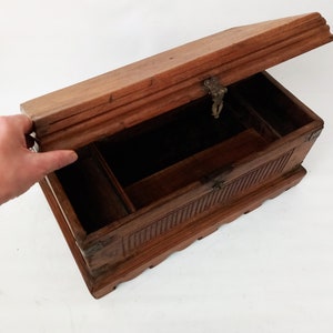 May include: A wooden box with a hinged lid and a brass latch. The box has intricate carvings on the front and sides. The box is open and the inside is empty.