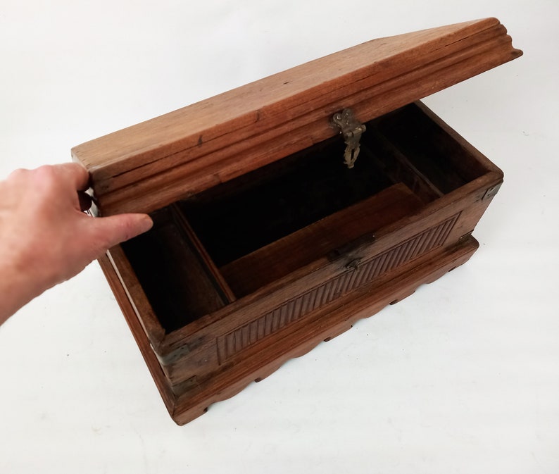 May include: A wooden box with a hinged lid and a brass latch. The box has intricate carvings on the front and sides. The box is open and the inside is empty.