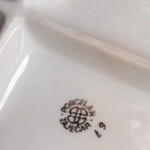 May include: White porcelain serving dish with multiple compartments. The dish has a glossy finish and a decorative emblem with the text "PORCELAN ZUECAR" in black. The number "6" is also visible.