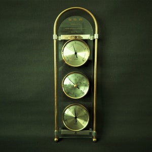 May include: A gold-colored weather station with three analog dials. The dials are labeled "Thermo-Hygro", "Barometer", and "Humidity".