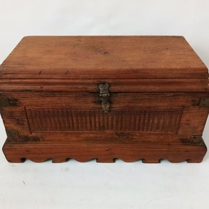 May include: A wooden chest with a hinged lid and brass accents. The chest has a carved design on the front and a decorative base.