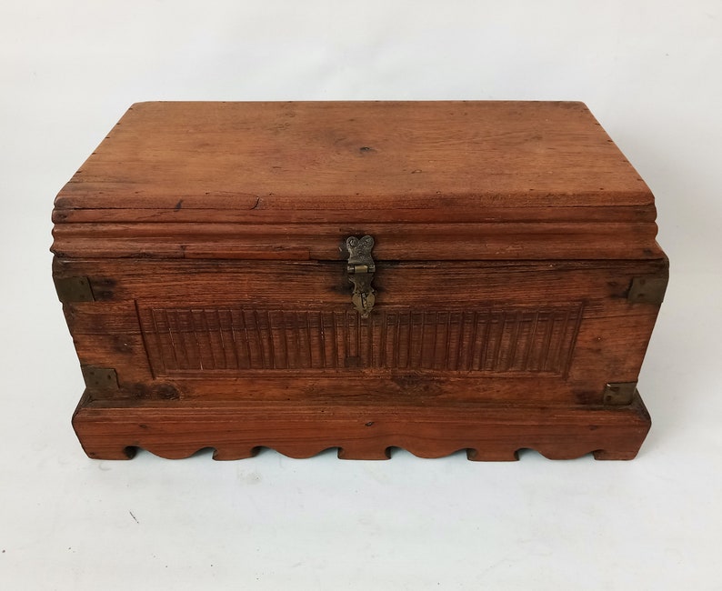 May include: A wooden chest with a hinged lid and brass accents. The chest has a carved design on the front and a decorative base.