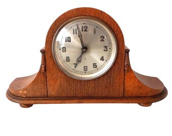 May include: A vintage wooden mantel clock with a white face and black hands. The clock has a Roman numeral clock face and is made of dark wood.