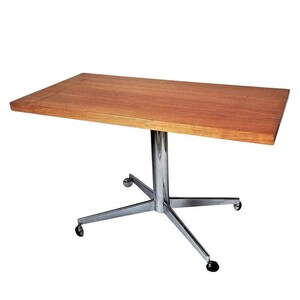 May include: A rectangular wooden table with a chrome base and four wheels. The table has a light wood finish and a simple design.