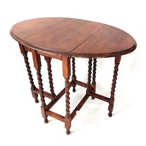 Op de afbeelding: Ovale antieke houten klaptafel. De tafel heeft een donkerbruine afwerking, een tweedelig tafelblad en ingewikkeld gesneden, spiraalvormige poten. Opengeklapt is de tafel ongeveer 91 cm lang.