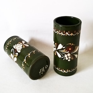 Op de afbeelding: Twee groene keramische bekers met witte en gouden bloemmotieven. De bekers zijn handgeschilderd en hebben een rustieke uitstraling.