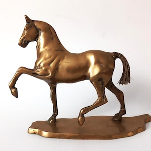 Può includere: Una scultura di cavallo color bronzo in posa rampante. Il cavallo ha una criniera e una coda dettagliate ed è montato su una base rettangolare. La scultura è in metallo e ha una finitura lucida.