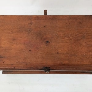 May include: A wooden box with a hinged lid and a metal latch. The box is made of dark brown wood and has a natural finish. The lid is closed and the box is sitting on a white surface.