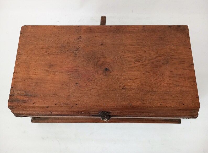 May include: A wooden box with a hinged lid and a metal latch. The box is made of dark brown wood and has a natural finish. The lid is closed and the box is sitting on a white surface.