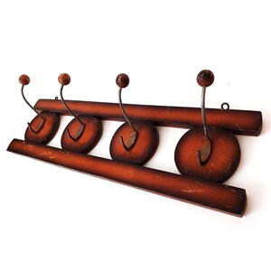 Op de afbeelding: Een houten kapstok met vier haken. De kapstok is bruin met een donkerbruine vlek. De haken zijn van metaal en zwart geverfd.
