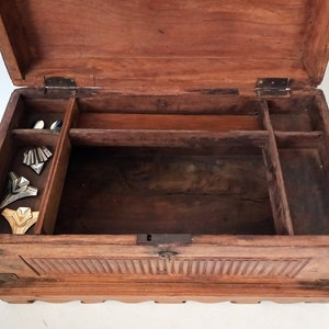 May include: An antique wooden box with a hinged lid and multiple compartments. The box is made of dark wood and has a carved design on the front. The inside of the box is empty.