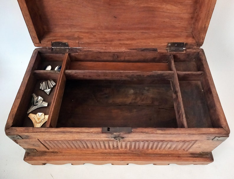 May include: An antique wooden box with a hinged lid and multiple compartments. The box is made of dark wood and has a carved design on the front. The inside of the box is empty.