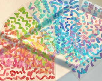 May include: Five sheets of rainbow-colored stickers with a variety of abstract shapes and designs. The stickers are translucent and have a glittery finish.