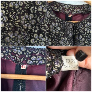 May include: A jacket featuring a black lace overlay with a metallic gold and purple floral pattern. The garment has a solid dark burgundy lining, a round neckline, and a tag displaying the number 44 along with a fabric composition label.
