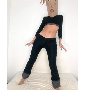 Peut inclure: Une personne portant un haut court à manches longues noir avec le mot "SISLEY" répété sur la bande. La personne porte également un jean noir avec les ourlets retroussés et un haut de bikini blanc.