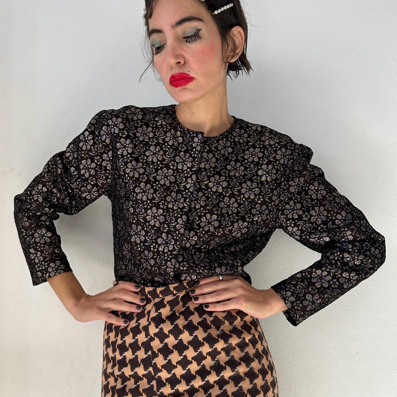 May include: A long-sleeved jacket featuring a black and metallic silver floral pattern with a round neckline and a front button closure, paired with a skirt displaying a brown and black houndstooth pattern that sits at the waistline.