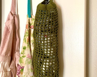 May include: A green crocheted produce bag hangs on a white hook. The bag is filled with plastic grocery bags. Two other fabric bags hang on hooks to the left.