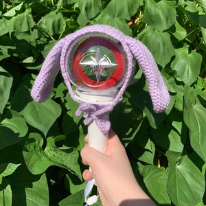 May include: Purple crocheted bunny ear hat for a light-up concert light stick with a red and white logo that says "Stray Kids".