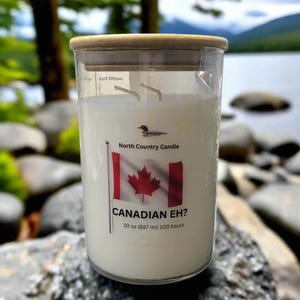 May include: A clear glass candle with a wooden lid. The candle has a white wax interior and a label featuring a Canadian flag and the text "CANADIAN EH?". The label also states "30 oz (887 ml) 100 hours".