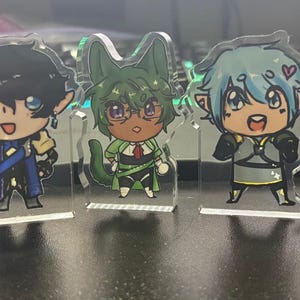 Puede incluir: Una fila de seis soportes acrílicos para personajes. Cada soporte presenta un personaje de anime de estilo chibi con diferentes colores de cabello, atuendos y expresiones. Los personajes están sobre bases transparentes, y el diseño es colorido y detallado.