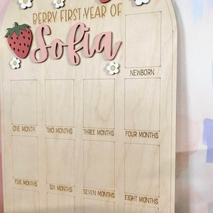 Puede incluir: Tablero de hitos de madera con el texto "Berry First Year of Sofia". El tablero presenta adornos de fresas y flores. Tiene espacios para fotos desde reci&eacute;n nacido hasta los once meses.