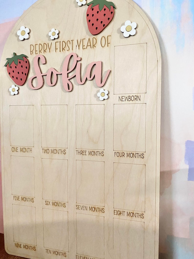 Puede incluir: Tablero de hitos de madera con el texto "Berry First Year of Sofia". El tablero presenta adornos de fresas y flores. Tiene espacios para fotos desde reci&eacute;n nacido hasta los once meses.