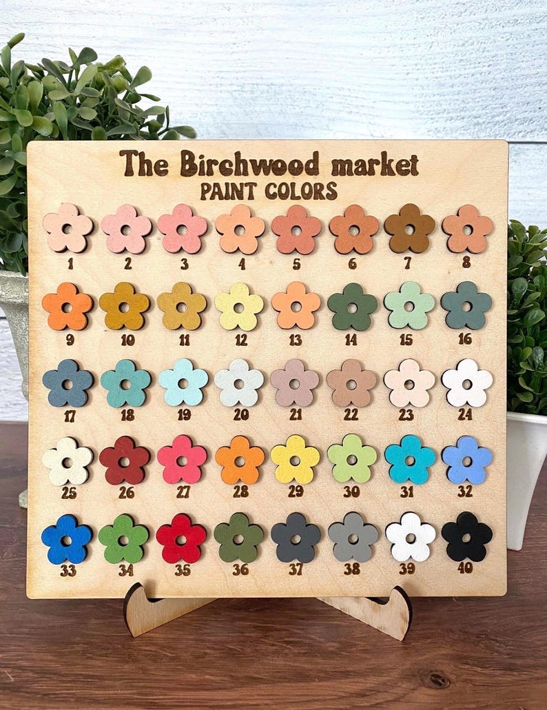 May include: A wooden display board with the text "The Birchwood market PAINT COLORS" features 40 flower-shaped paint color samples. The colors range from light pink to dark brown, with various shades of blue, green, and orange.
