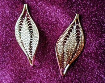May include: A pair of gold leaf-shaped earrings with a delicate, intricate design. The earrings are made of a fine wire mesh and have a slightly curved shape.