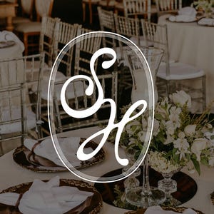 Könnte beinhalten: Elegante Hochzeitstafel mit weißen Tischdecken, goldgeränderten Tellern und Blumengestecken. Das Bild zeigt ein weißes ovales Logo mit den Buchstaben "S" und "H" in Schreibschrift, was auf eine personalisierte Veranstaltung hindeutet.
