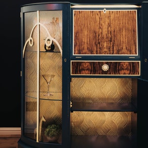May include: A dark blue wooden cabinet with glass doors and shelves. The cabinet has a gold trim and a patterned wallpaper lining the shelves. The cabinet has a closed wooden door on the right side.