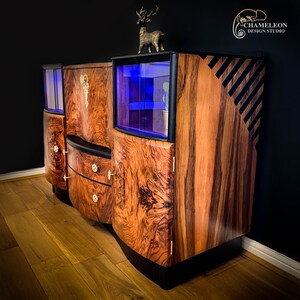 May include: A vintage wooden cabinet with glass doors and drawers. The cabinet has a dark wood finish with a unique grain pattern. The cabinet has a black trim and a deer figurine on top.