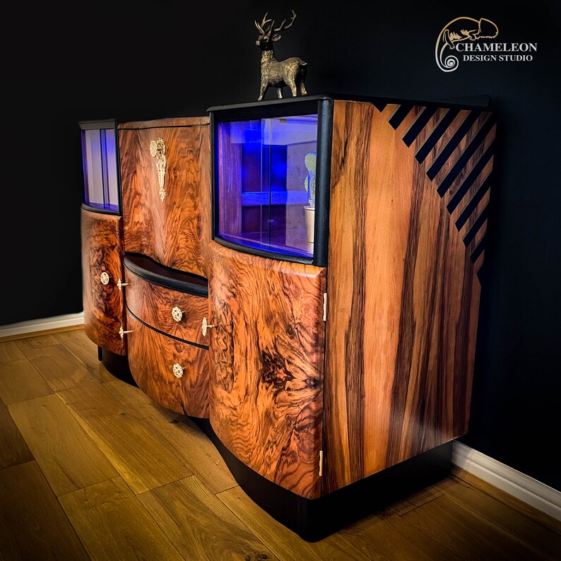May include: A vintage wooden cabinet with glass doors and drawers. The cabinet has a dark wood finish with a unique grain pattern. The cabinet has a black trim and a deer figurine on top.