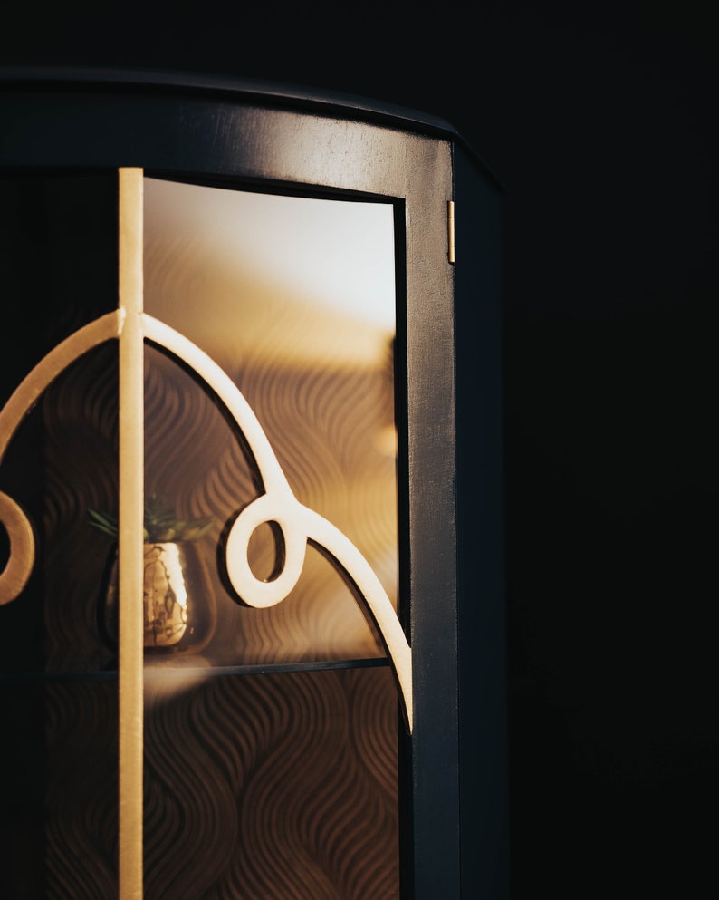 May include: A dark blue cabinet with a glass door and gold accents. The glass door has a decorative pattern and a small plant is visible inside.