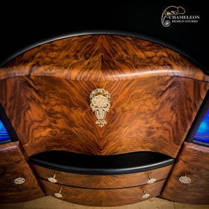 May include: A curved wooden cabinet with two drawers and a decorative metal handle. The cabinet is made of dark wood with a rich grain pattern. The drawers have black leather trim and gold-colored handles.