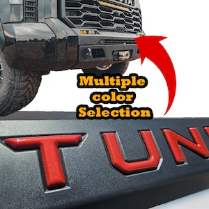 May include: Close-up of a black truck bumper with red lettering that spells out "TUNDRA". The image also includes the text "Multiple color Selection" in yellow and black.