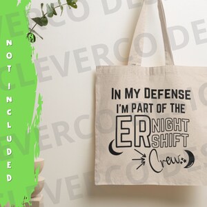 May include: A white canvas tote bag with black text that reads "In my defence I'm part of the ER Night Shift Crew." The text is styled with a crescent moon and a star on either side of the text.