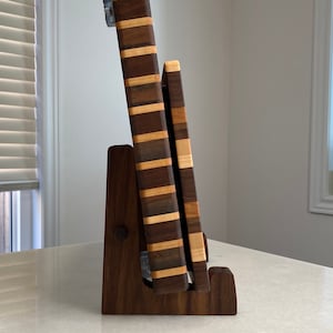 May include: A wooden cutting board set with a stand. The boards are made of alternating dark and light wood strips. The stand is a dark brown color and holds the boards upright. The set is displayed on a white surface.