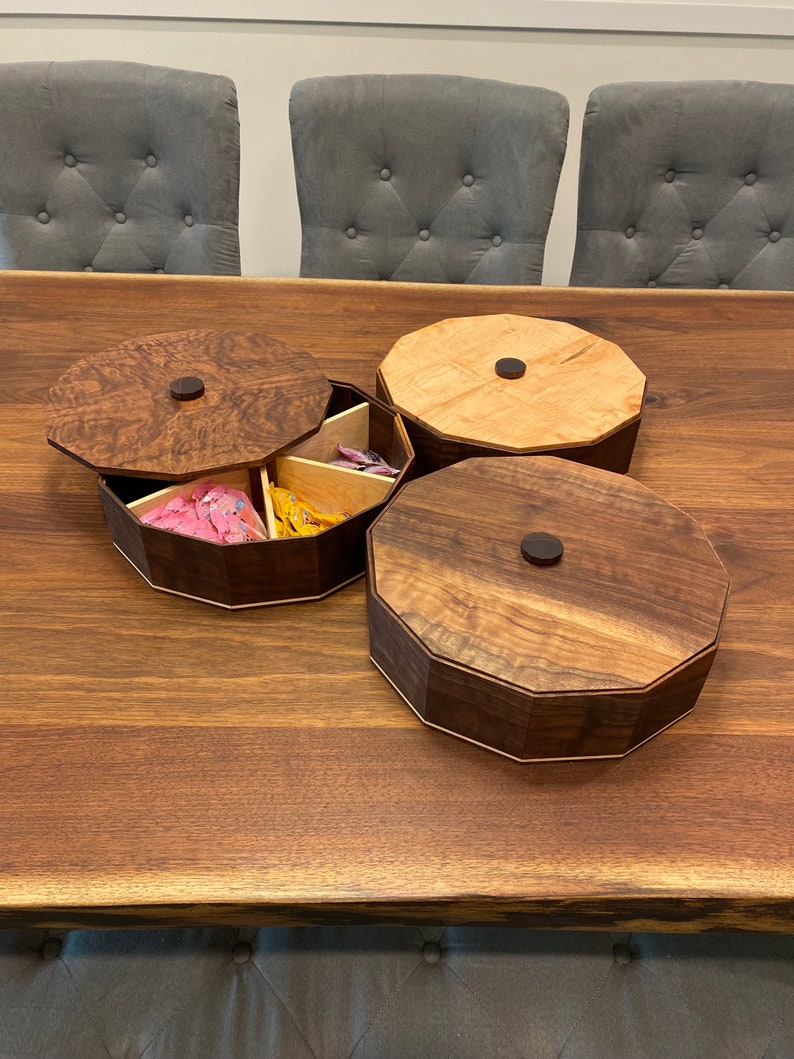 May include: Three wooden octagonal boxes with lids. The boxes are made of different types of wood, including walnut and maple. The boxes are arranged on a wooden table.