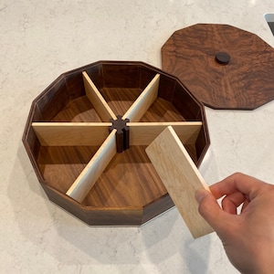 May include: A wooden octagonal box with a lid, divided into six compartments. The box is made of walnut wood with maple wood dividers. The lid is also made of walnut wood and has a small knob on top.