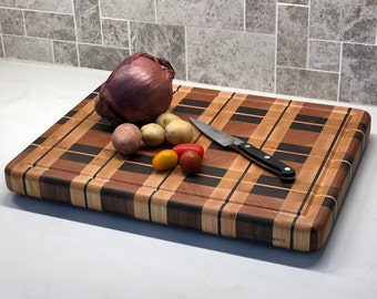 May include: A large wooden cutting board with a checkered pattern in shades of brown, red, and black. The board has a raised edge and is decorated with a small logo that reads "GAN STUDIO". The board is topped with a red onion, four small potatoes, and five red cherry tomatoes.