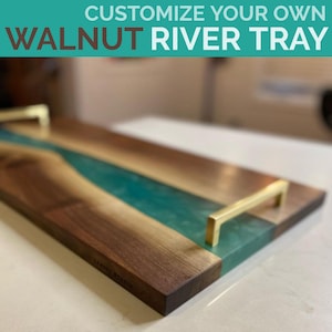 May include: A walnut wood serving tray with a teal blue resin river inlay and gold metal handles. The tray is handcrafted and has a natural wood finish.