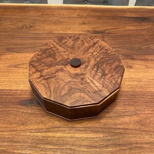 May include: A wooden octagonal box with a dark brown finish and a small wooden knob on the lid.